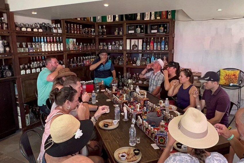 Un gruppo di persone sedute a un tavolo in un bar, con scaffali pieni di bottiglie sullo sfondo. 1