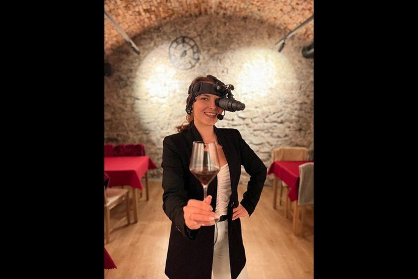 Una persona sostiene una copa de vino en un comedor rústico con paredes de piedra y manteles rojos. 5