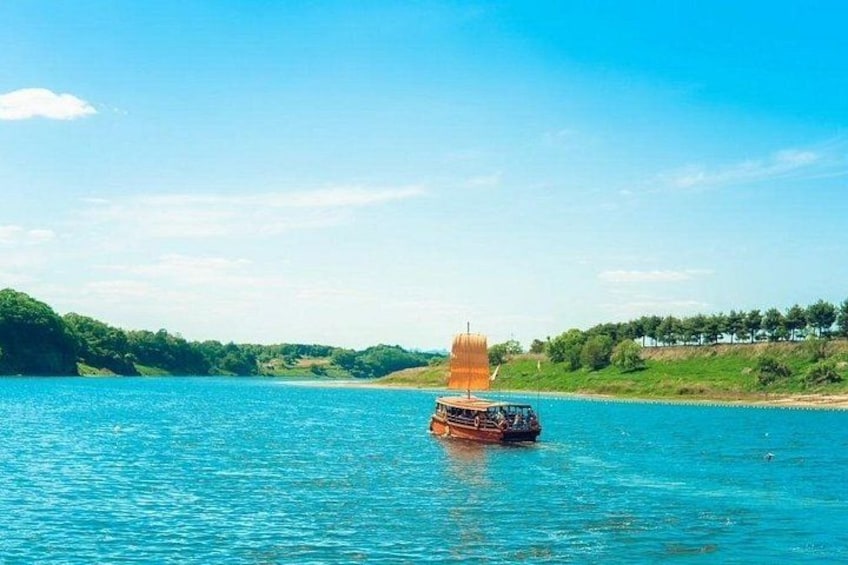 A sailboat on a calm blue sea with a green shoreline and trees in the background. 2
