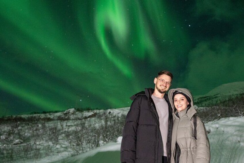 Two people standing in a snowy landscape with the Northern Lights in the background. 3