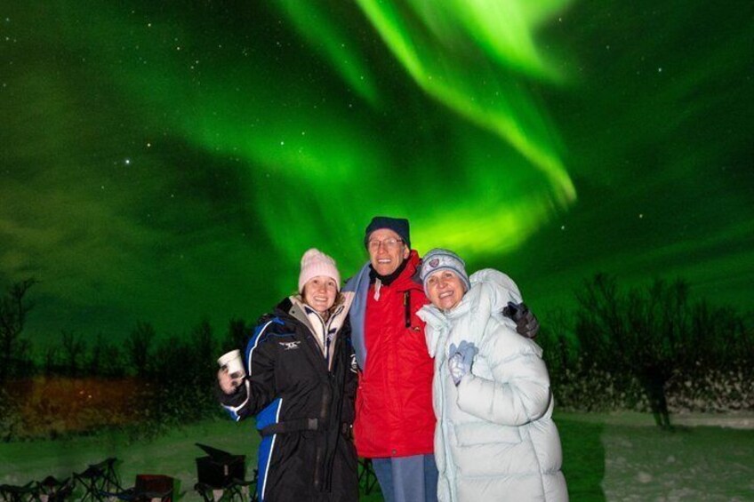 Three people posing under the Northern Lights. 4