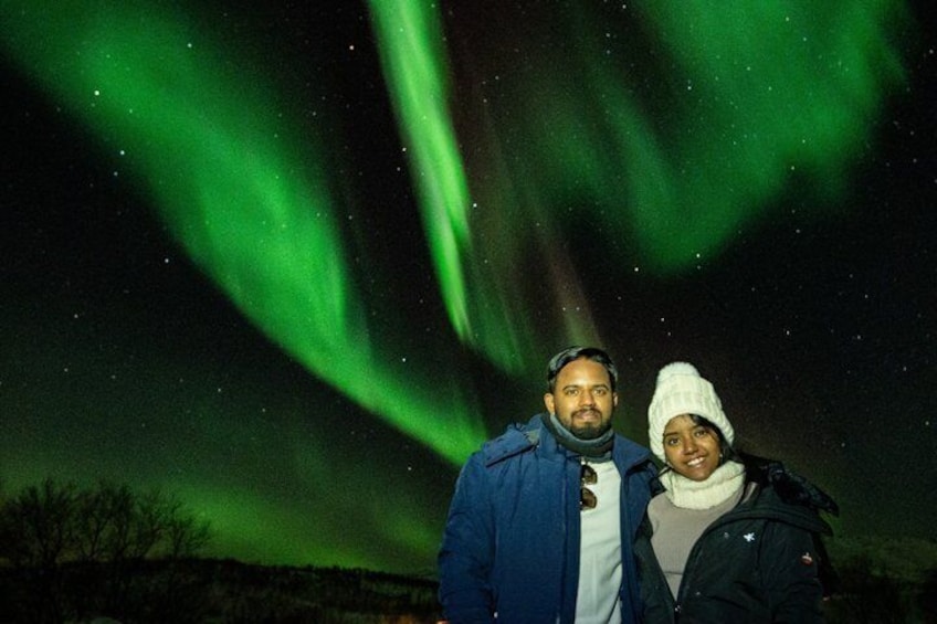 Two people standing under a night sky with green aurora borealis. 5