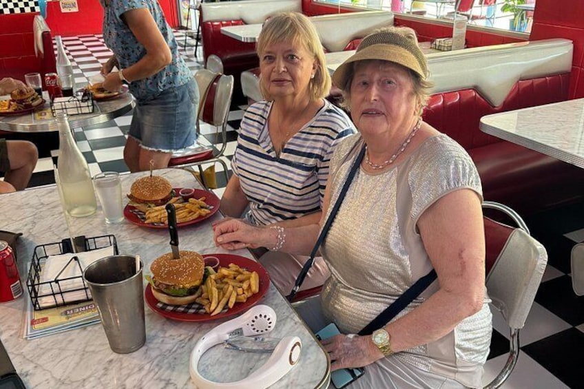 Two people sitting at a table with burgers and fries, a menu, and a drink. 5