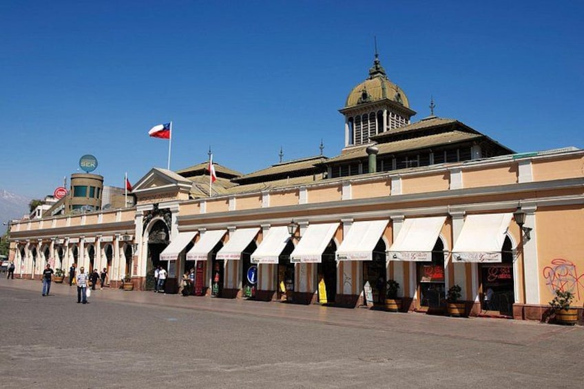 A historic building with a dome and flags, a wide street, and outdoor seating areas. 2