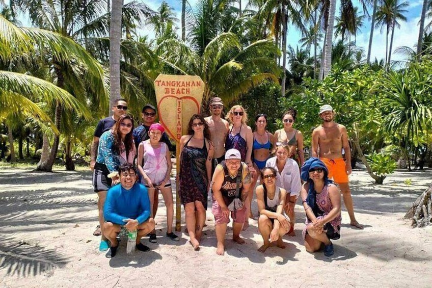 A group of people posing in front of a sign that reads 'TANGKAHAN BEACH ISLAND.' 2