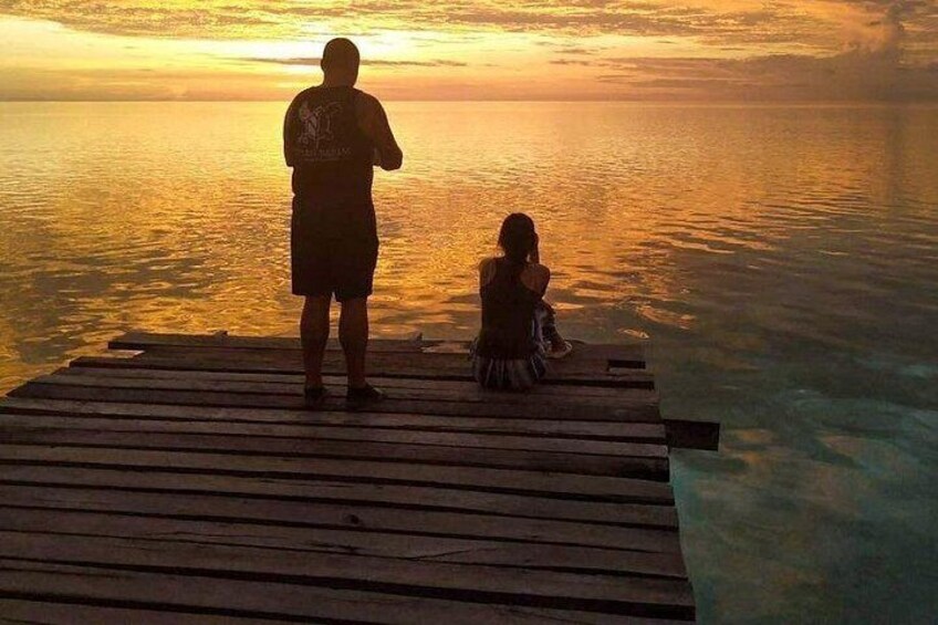 Two people on a wooden dock overlooking a body of water during sunset. 3