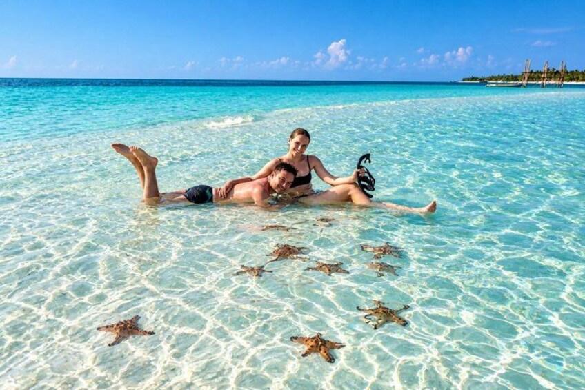 Two people lying on a beach with clear turquoise water and starfish. 1