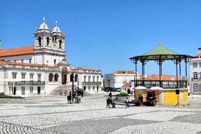 A historic building with a bell tower, a gazebo, and cobblestone pavement. 2