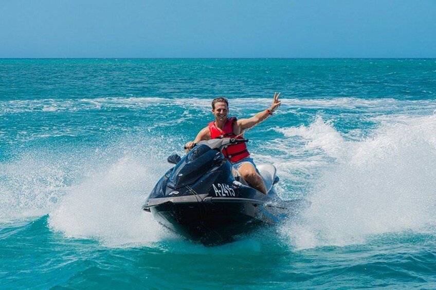 A person riding a jet ski on turquoise water with waves around the jet ski. 1