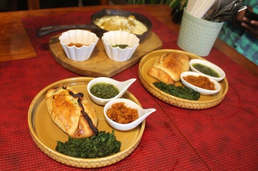 Un plato con dos fuentes de comida, incluyendo un muslo de pollo relleno y un guiso de verduras, acompañado de recipientes pequeños con salsas. 5