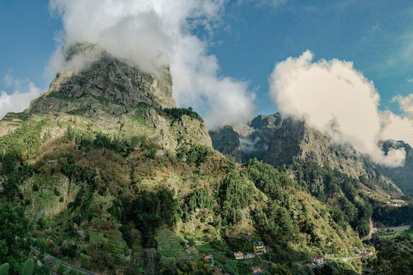 Un paysage montagneux caractérisé par une végétation luxuriante, un sommet rocheux imposant et une vallée parsemée de bâtiments. 1