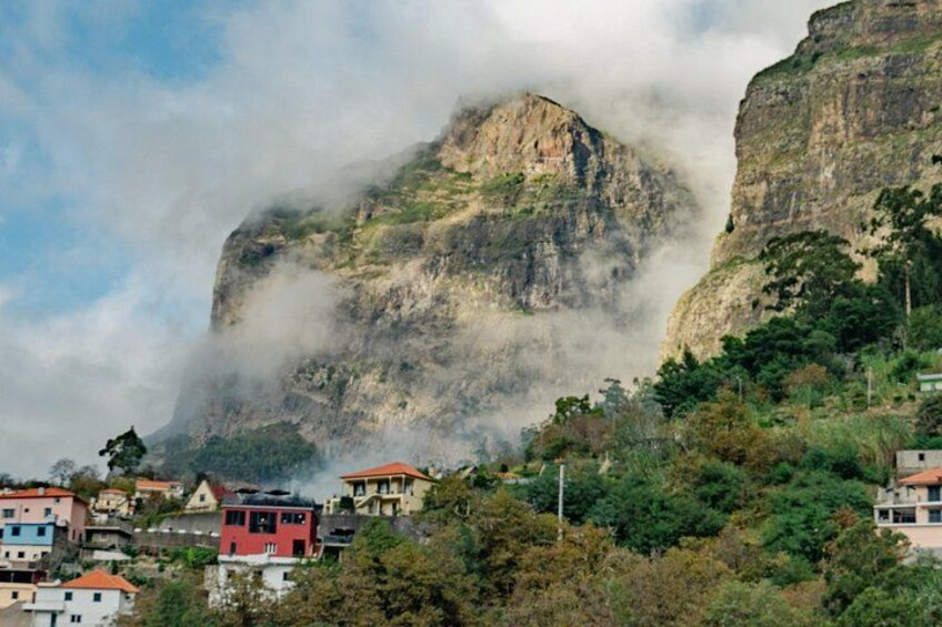 Un paysage montagneux dominé par un sommet imposant enveloppé de nuages, entouré d’un quartier résidentiel aux maisons aux couleurs vives. 4