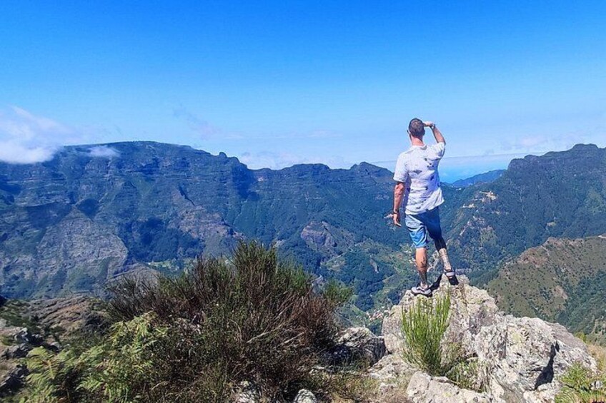 Une personne se tient debout sur un promontoire rocheux, d’où elle domine un paysage montagneux. 2