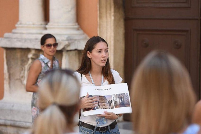 Una persona tiene in mano un libretto con la scritta 'St. Simon Church' davanti a un edificio con colonne. 2