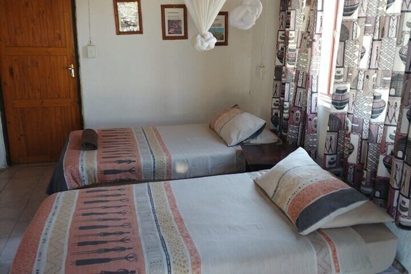 A room with two beds, patterned curtains, and a wooden door. 1