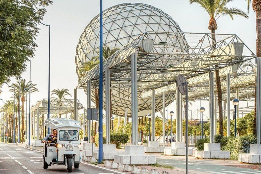 Una calle con una estructura de vidrio esférica, un triciclo y palmeras. 4