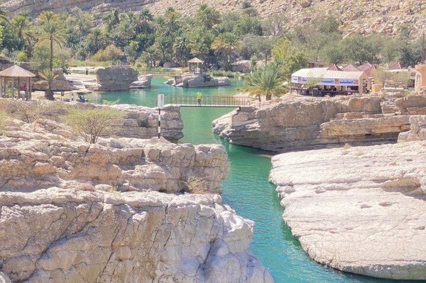 Un paysage rocheux avec une piscine aux eaux turquoise, des palmiers et un bâtiment surmonté d’un toit rouge. 2