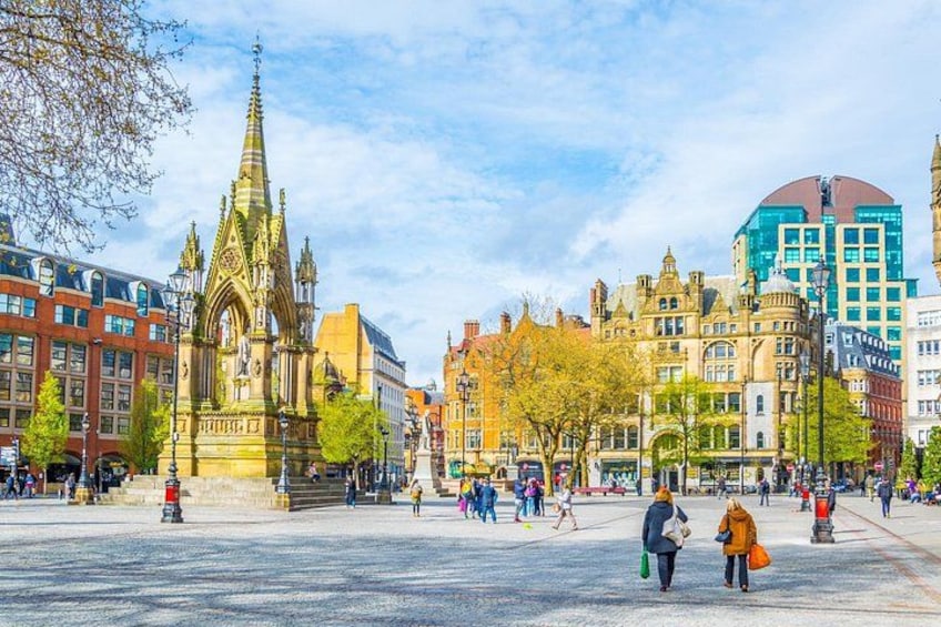 Ett historiskt torg med ett markant kyrktorn, en modern byggnad och fotgängare. 5