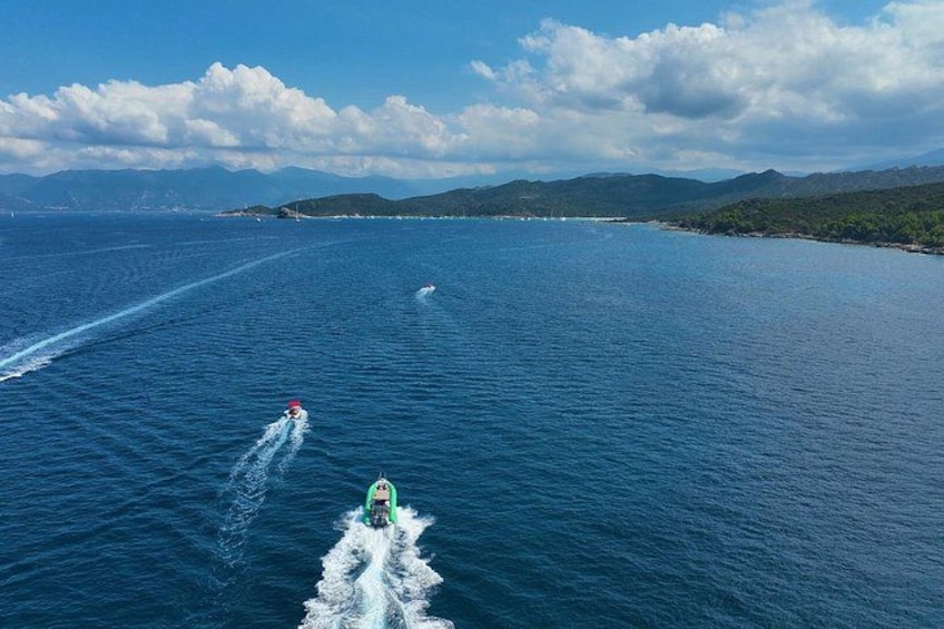 A green speedboat with a wake behind it, a person in a red life jacket, and a coastline with mountains in the background. 2