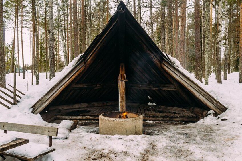 A snow-covered wooden structure with a fire in the center, surrounded by a forest. 3