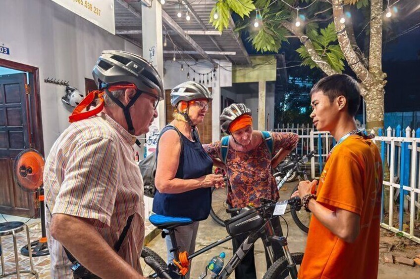 A group of people with bicycles, a tree, and a white fence in an outdoor setting. 5