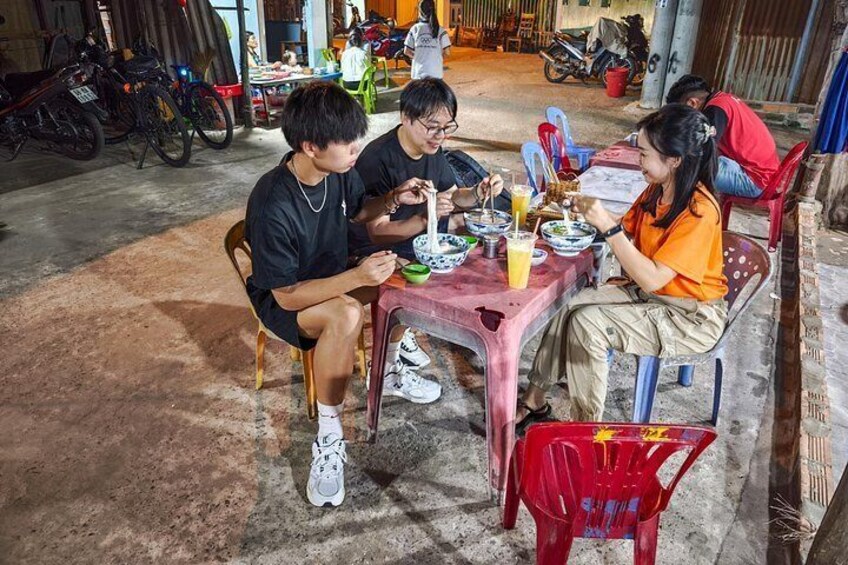 Three people sitting at a table with food and drinks, in a room with motorcycles and bicycles in the background. 2