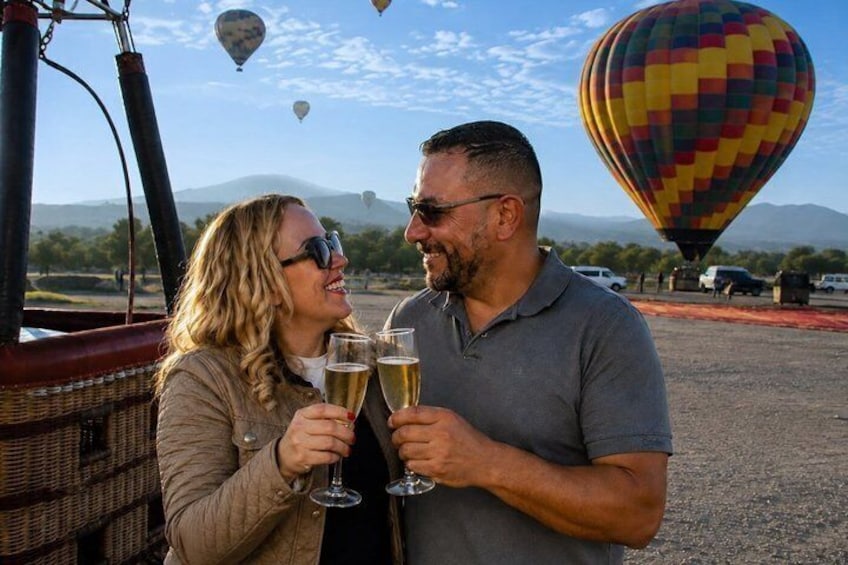A couple toasting with champagne glasses, a hot air balloon in the background, and a scenic landscape with mountains. 5