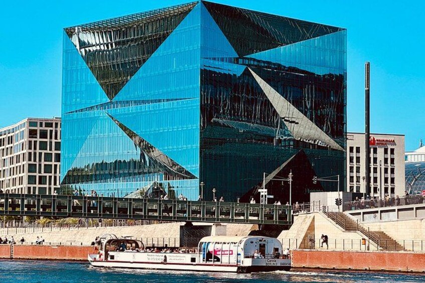 A modern glass building with a unique geometric design, a boat on the water in front, and a clear blue sky. 4