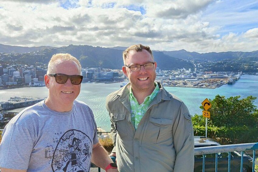 Two people standing with a cityscape and a river in the background. 2