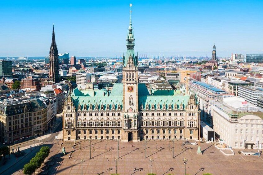 A large historic building with a prominent tower and green roof, surrounded by other city buildings. 5