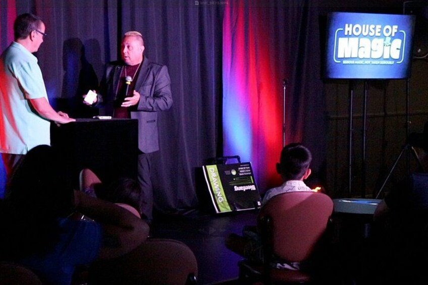 A stage with a podium, a microphone, and a screen displaying 'HOUSE OF MAGIC'. 2