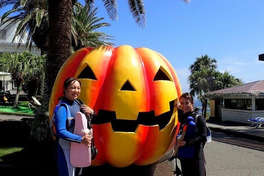Two people standing next to a large pumpkin decoration with a carved face. 3
