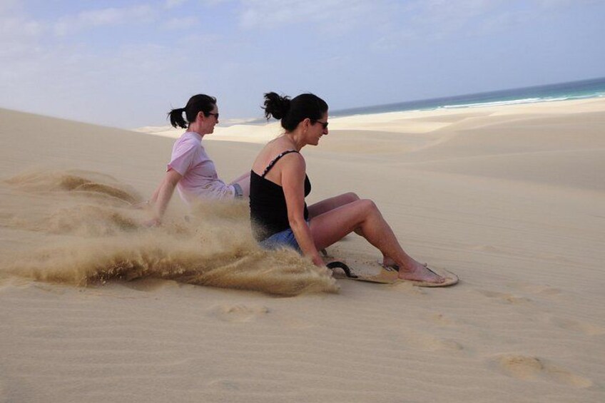 Twee personen zitten op het strand, met zandduinen op de achtergrond. 5