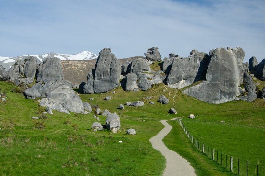 A pathway leading through a grassy area with large rock formations and a mountain in the background. 1