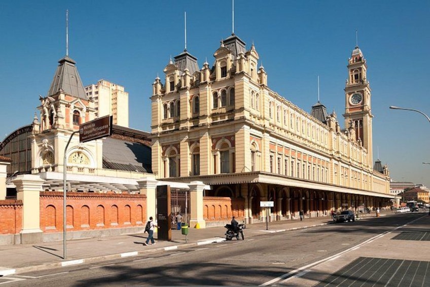 A large, ornate building with a clock tower, a covered walkway, and a street with a few pedestrians and vehicles. 4