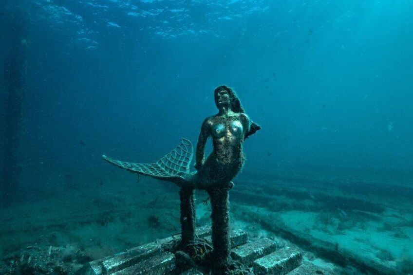 An underwater statue of a mermaid with a tail, surrounded by a shipwreck. 2