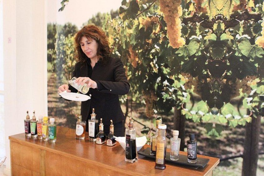 A person pouring a liquid from a bottle into a glass on a wooden counter with various bottles and containers. 1