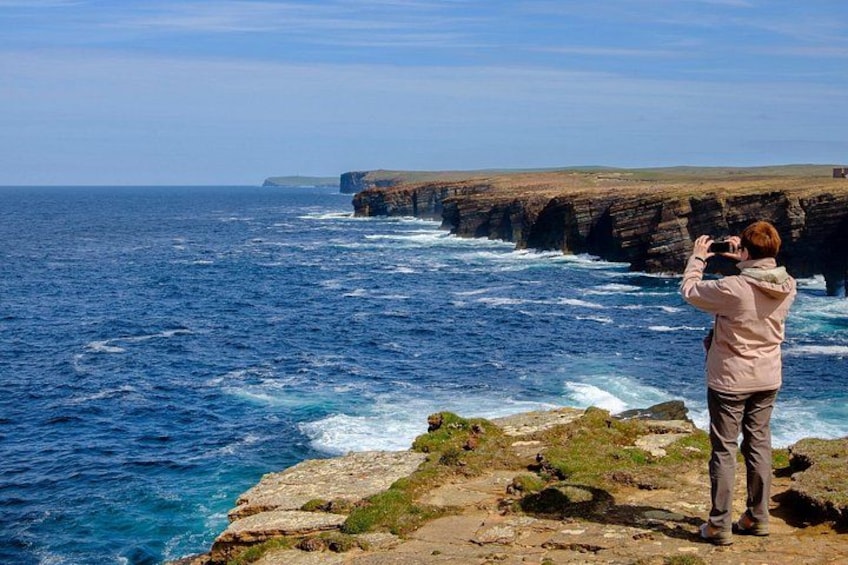 A person taking a photo of a coastal landscape with cliffs and the ocean. 2