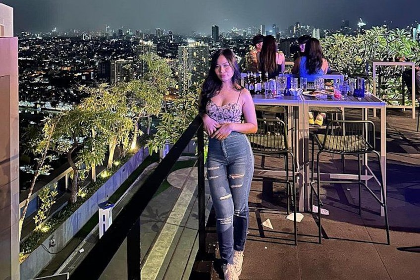 Una mujer parada en un balcón con vistas a un paisaje urbano nocturno. 3