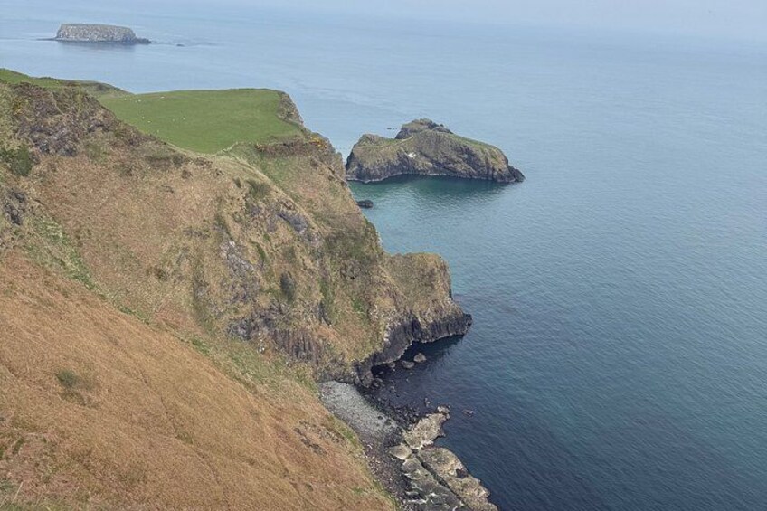 A coastal landscape with grassy cliffs, rocky outcrops, and calm sea. 4