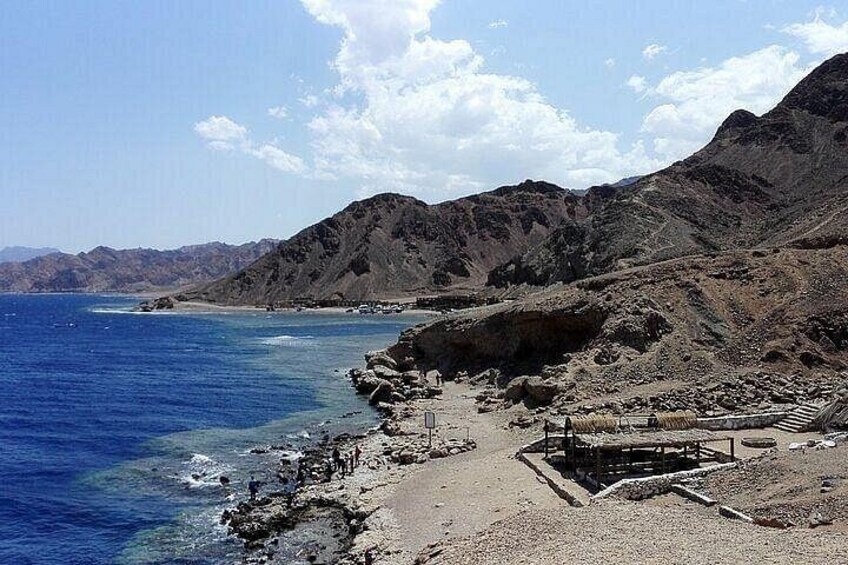 A coastal landscape with a rocky beach, clear blue sea, and distant mountains. 5