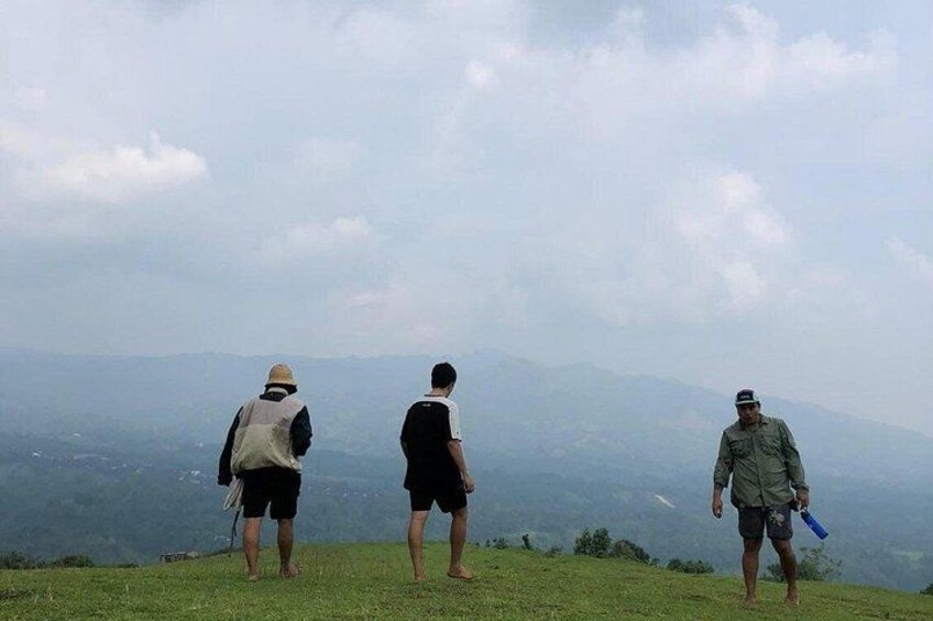 Three people standing on a grassy hill overlooking a mountainous landscape. 2