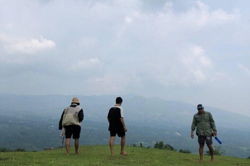 Tres personas están de pie en una colina cubierta de hierba, con vistas a un paisaje montañoso. 2