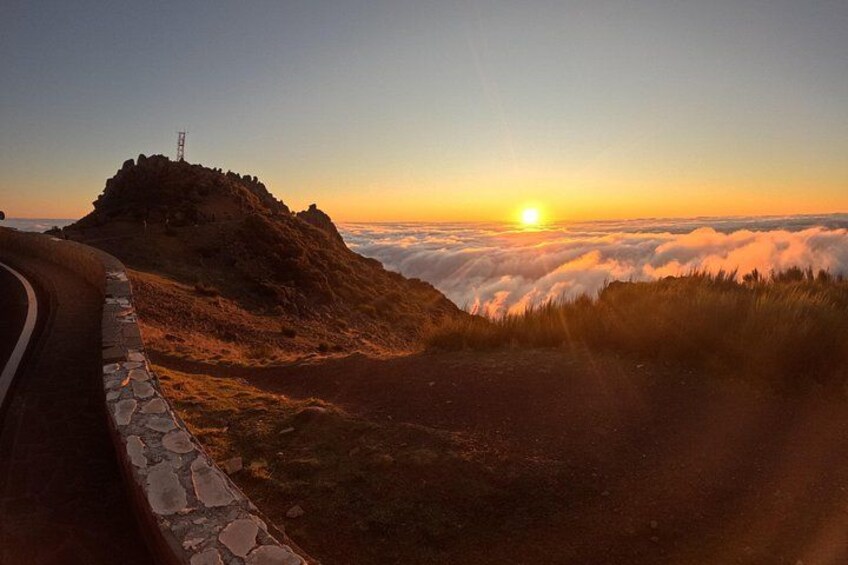 A sunrise over a mountain with a road curving around it. 2