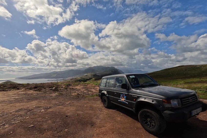 A vehicle parked on a dirt road with a coastal landscape in the background. 3