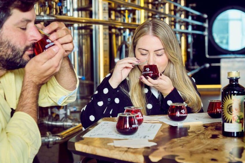 Two people tasting red wine at a bar with a wooden table, wine glasses, and bottles. 3