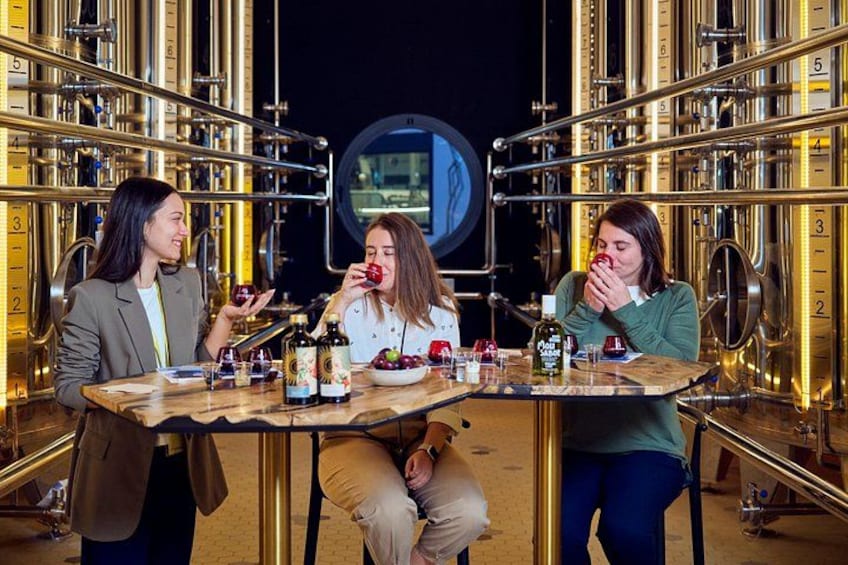 Three people tasting food at a table in a room with brass instruments. 1