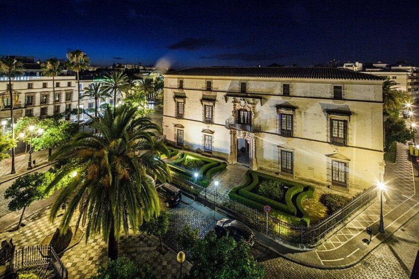 A historic building with a courtyard, palm trees, and street lamps. 1