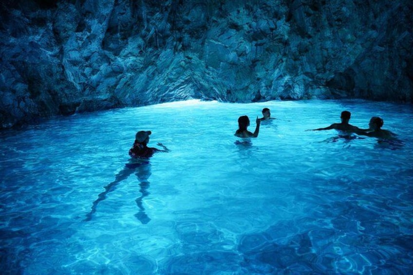 A group of people in a blue-lit swimming pool with rocky walls. 4