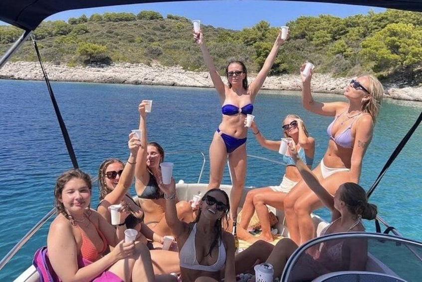 A group of people on a boat, some holding drinks, with a body of water and greenery in the background. 3